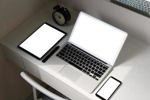 il computer portatile dello schermo in bianco e lo Smart Phone e la penna digitale dello stilo e della compressa è sullo scrittorio di legno come concetto del posto di lavoro foto