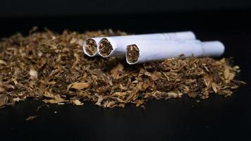 mucchio di tabacco e qualche sigaretta su sfondo nero foto