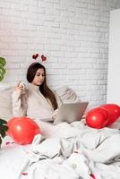 giovane bella donna seduta nel letto per celebrare il giorno di San Valentino lavorando sul computer portatile
