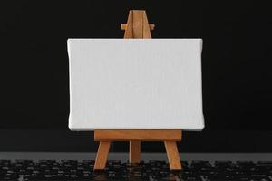 tela bianca e cavalletto di legno sul computer portatile come concetto foto