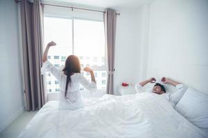 amante delle coppie che si sveglia nel suo letto completamente riposato e apre le tende al mattino per prendere aria fresca. foto