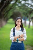 bella studentessa asiatica che tiene libri e sorride alla macchina fotografica e concetto di apprendimento e istruzione sul parco in estate per rilassarsi foto