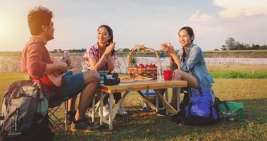 un gruppo di amici asiatici che giocano a ukelele e passano il tempo a fare un picnic durante le vacanze estive. Sono felici e si divertono in vacanza. foto