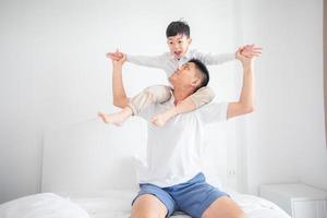 felice famiglia asiatica con figlio a casa in camera da letto che gioca e ride foto