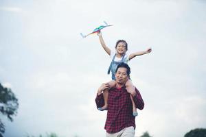 bambina asiatica e padre con un aquilone che corre e felice sul prato in estate nella natura foto