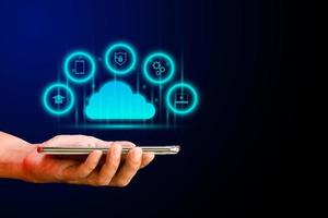 concetto di archiviazione dei dati della tecnologia di cloud computing. mano che tiene smartphone o cellulare con cloud e icona virtuale e business, istruzione, innovazione su sfondo blu scuro. foto