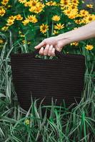 la mano della donna che tiene una borsa a maglia marrone su uno sfondo di erba e fiori. copia, spazio vuoto per il testo foto