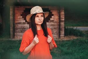 bella donna con un cappello di paglia vestito di rosso si erge sullo sfondo di una casa di legno foto