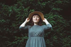 donna con un cappello di paglia e vestito con gli occhi chiusi su uno sfondo di foresta verde e alberi foto