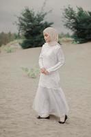 bella modella islamica che indossa la moda hijab, un moderno abito da sposa per donna musulmana cammina lungo la sabbia e il mare. una modella asiatica che usa l'hijab divertendosi in spiaggia. prematrimonio fotografico foto