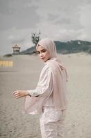 bella modella islamica che indossa la moda hijab, un moderno abito da sposa per donna musulmana cammina lungo la sabbia e il mare. una modella asiatica che usa l'hijab divertendosi in spiaggia. prematrimonio fotografico foto