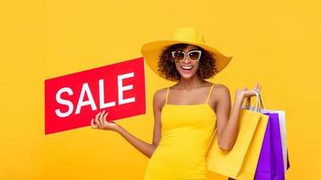 donna sorpresa capelli ricci alla moda che trasportano borse della spesa con segno di vendita rosso su sfondo giallo foto