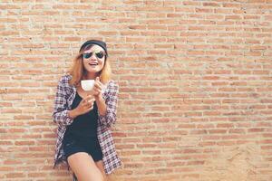 donna allegra in strada che beve il caffè del mattino contro il muro di mattoni. foto