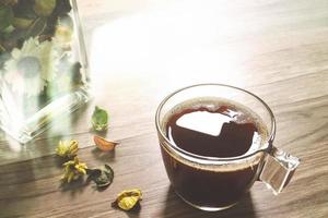 tazza di caffè o tè, vaso di vetro erbe aromatiche secche, su tavola di legno, effetto filtro, primo piano foto