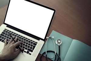 vista dall'alto della mano del medico di medicina che lavora con il computer moderno e lo schermo vuoto sulla scrivania di legno come concetto medico foto