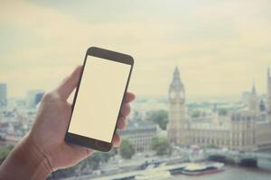 mano dell'uomo che tiene lo smartphone con schermo vuoto contro lo sfondo sfocato della città di Londra foto