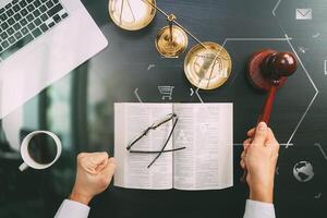 concetto di giustizia e diritto.vista dall'alto della mano del giudice maschio in un'aula di tribunale con il martello e la scala di ottone e il computer e il libro della Bibbia aperta su un tavolo di legno scuro con diagramma vr foto