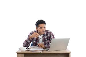 giovane premuroso che guarda il computer portatile mentre è seduto al suo posto di lavoro isolato su sfondo bianco. foto
