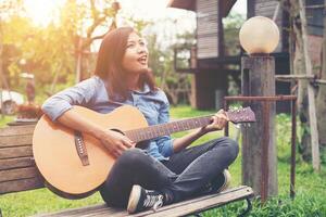 bella giovane donna che suona la chitarra seduta su una panchina, concetto di tempo felice. foto