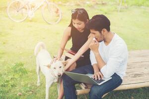 giovane coppia di educazione seduta sulla panchina gioca con il cane all'aria aperta e il bel tempo. e sono felici, concetto di stile di vita. foto