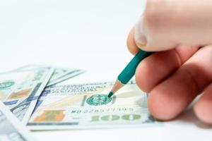 disegnare soldi. un botto in mano tiene una matita su una banconota da cento dollari. foto