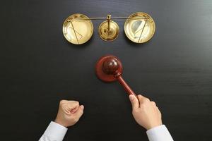 concetto di giustizia e diritto. Vista dall'alto della mano del giudice maschio in un'aula di tribunale con il martello e la scala di ottone su un tavolo di legno scuro foto