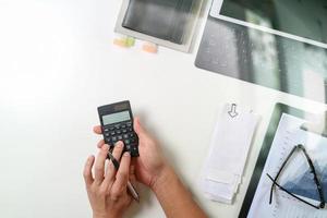 vista dall'alto della mano dell'uomo d'affari che lavora con le finanze su costi e calcolatrice e computer portatile con il telefono cellulare sulla scrivania bianca in un ufficio moderno foto