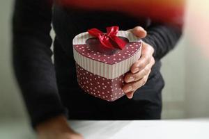 regalo, mano d'uomo che tiene una confezione regalo in un gesto di dare. sfondo sfocato, effetto vintage foto