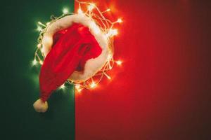 concetto di stagione dei saluti. Cappello di Babbo Natale con luce di Natale su sfondo rosso e verde foto