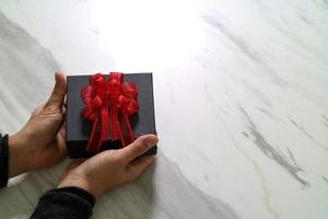 regalo, mano d'uomo che tiene una confezione regalo in un gesto di dare su sfondo bianco tavolo in marmo grigio foto