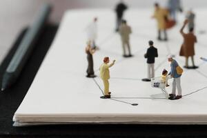 primo piano di persone in miniatura con diagramma di rete sociale su notebook aperto su scrivania in legno come concetto di social media foto