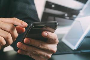 primo piano della mano dell'uomo d'affari che lavora con smartphone e laptop e computer tablet digitale in un ufficio moderno foto