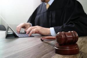 concetto di giustizia e diritto. giudice maschio in un'aula di tribunale con il martelletto, lavorando con la tastiera di aggancio del computer tablet digitale su un tavolo di legno foto