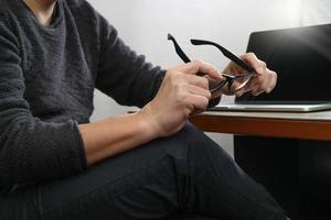 progettista del sito Web che tiene il computer portatile del computer di lavoro degli occhiali sul tavolo di legno foto