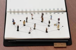 primo piano di persone in miniatura con diagramma di rete sociale su notebook aperto su scrivania in legno come concetto di social media foto