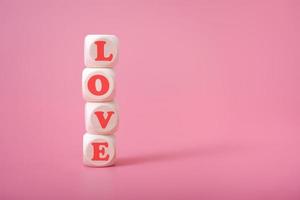 la parola amore è a forma di cuore su cubi di legno su sfondo rosa. foto