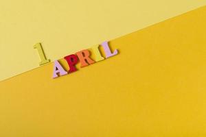 lettere di legno il primo aprile su sfondo giallo. il concetto di vacanza, foto