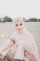 bella modella islamica che indossa la moda hijab, un moderno abito da sposa per donna musulmana seduta sulla sabbia e sulla spiaggia. ritrarre un modello di ragazza asiatica usando l'hijab divertendosi in spiaggia con alberi foto