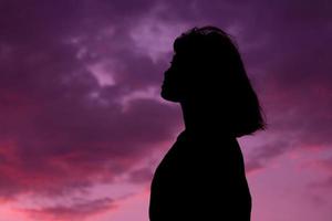 silhouette colpo medio di donna o donna in piedi con lo sfondo del tramonto del cielo sull'ora del tramonto. foto