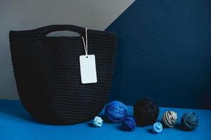 borsa fatta a mano in maglia nera con gomitoli di filo su sfondo blu e grigio. copia, spazio vuoto per il testo foto