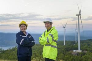 ritratto di persone ingegnere sono in piedi in un campo indossando un casco protettivo sulla testa su sfondo di turbine elettriche. foto