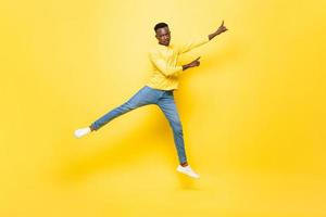 giovane uomo africano energico che salta e punta le mani in alto su sfondo giallo isolato per studio foto