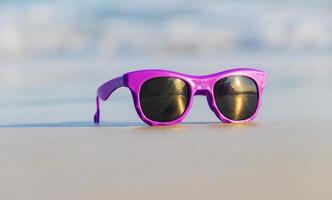 occhiali da sole viola moda sulla sabbia bellissima spiaggia estiva foto