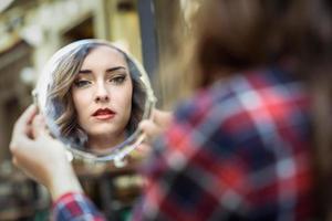 giovane donna che si guarda in un piccolo specchio foto