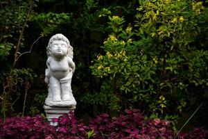 statuetta bianca di un angelo in piedi e baciare in giardino di casa il giorno foto