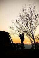 sagoma di madre con sua figlia vicino alla tenda e albero al tramonto foto