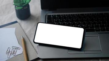 modello di mockup di telefono cellulare con schermo bianco su un laptop per il lavoro a distanza e il concetto di home office foto