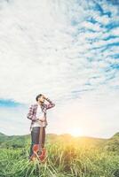 giovane uomo hipster che tiene una chitarra con una passeggiata nella natura, rilassante nel campo in una giornata di sole con cielo blu. foto