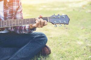 il giovane uomo hipster si esercitava con la chitarra nel parco, felice e si divertiva a suonare la chitarra. foto