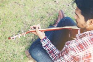 il giovane uomo hipster si esercitava con la chitarra nel parco, felice e si divertiva a suonare la chitarra. foto